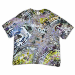 An artisanal ice-dyed t-shirt, its surface a canvas of swirling blues, purples, and chartreuse resembling geode formations, with the text 'dazed' in a stylized, icy lettering at the center.