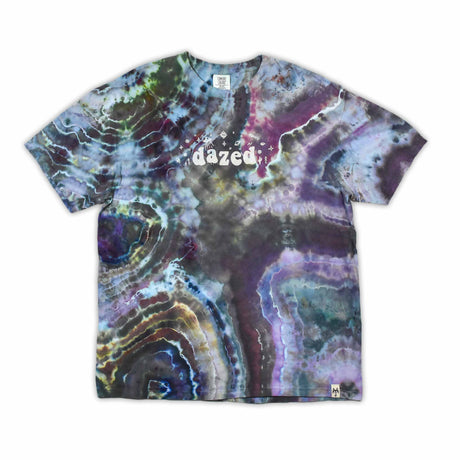 The vibrant patterns of this tie-dye t-shirt are reminiscent of a sliced geode, with bands of blue, purple, and green that encircle the 'dazed' text, which glistens like a quartz inscription.