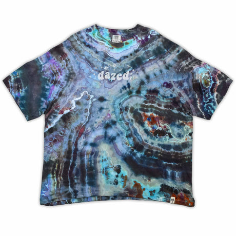 The vibrant patterns of this tie-dye t-shirt are reminiscent of a sliced geode, with bands of blue, purple, and green that encircle the 'dazed' text, which glistens like a quartz inscription.