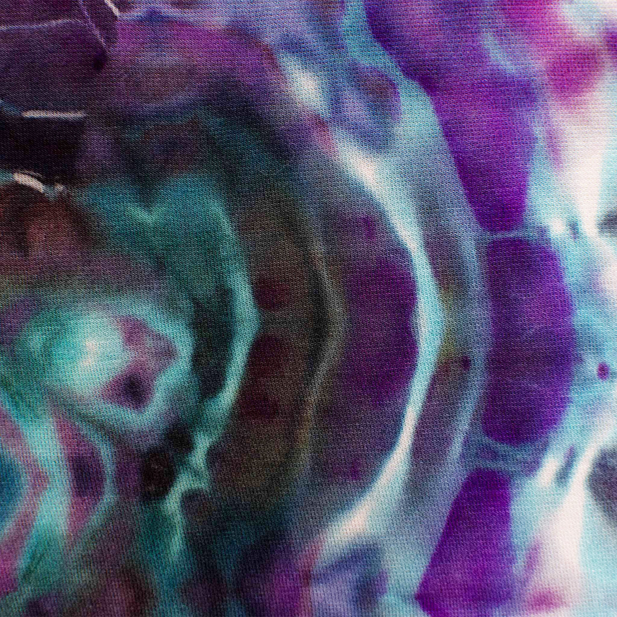 A pair of hand-dyed pants showcasing a unique ice-dye technique with organic patterns in a striking combination of sapphire, violet, and seafoam green.