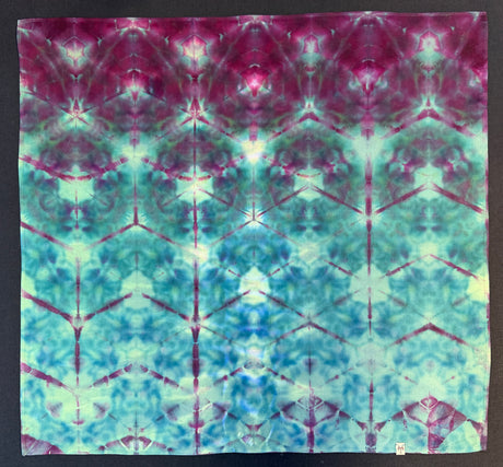 A 100% Cotton Bandana with a symmetrical tie-dye pattern in magenta, teal, aqua, and pale green, photographed flat against a dark background.