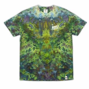 The 'Dinkey Creek' logo is subtly placed on a t-shirt with a mottled ice dye pattern in shades of green and purple, mimicking the natural variations of foliage. Features a unique 'Dinkey Creek' screen print design.