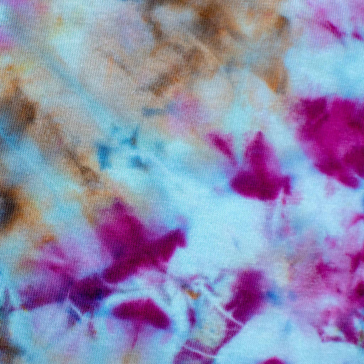 A t-shirt featuring a symmetrical ice dye pattern with a vibrant explosion of sapphire blues and fuchsia pinks against a soft blue background.