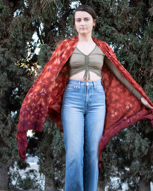 A richly colored shawl with an intricate pattern of deep red and orange hues is elegantly draped over the shoulders, catching the light and adding a luxurious layer to the attire.