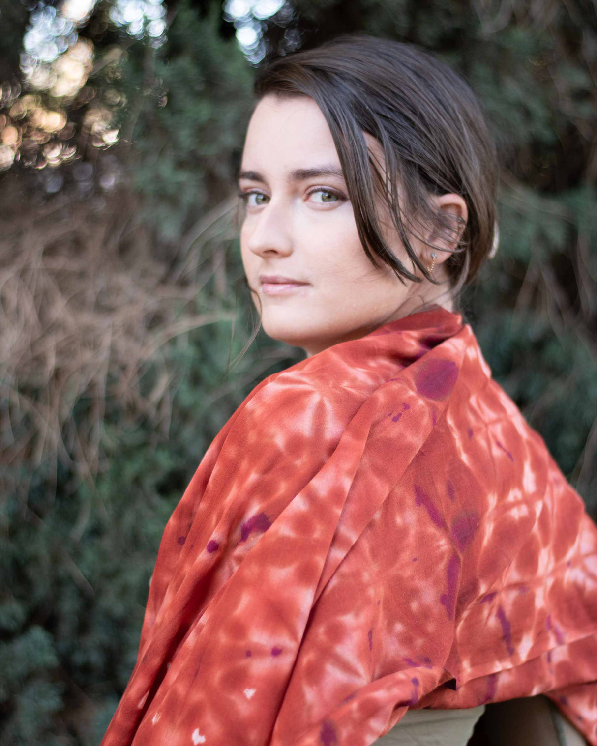 A richly colored shawl with an intricate pattern of deep red and orange hues is elegantly draped over the shoulders, catching the light and adding a luxurious layer to the attire.