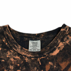 A stylish bleached t-shirt makes a statement with the 'Woof Dyes' logo, amidst a mottled backdrop of blacks and browns for a rugged look.